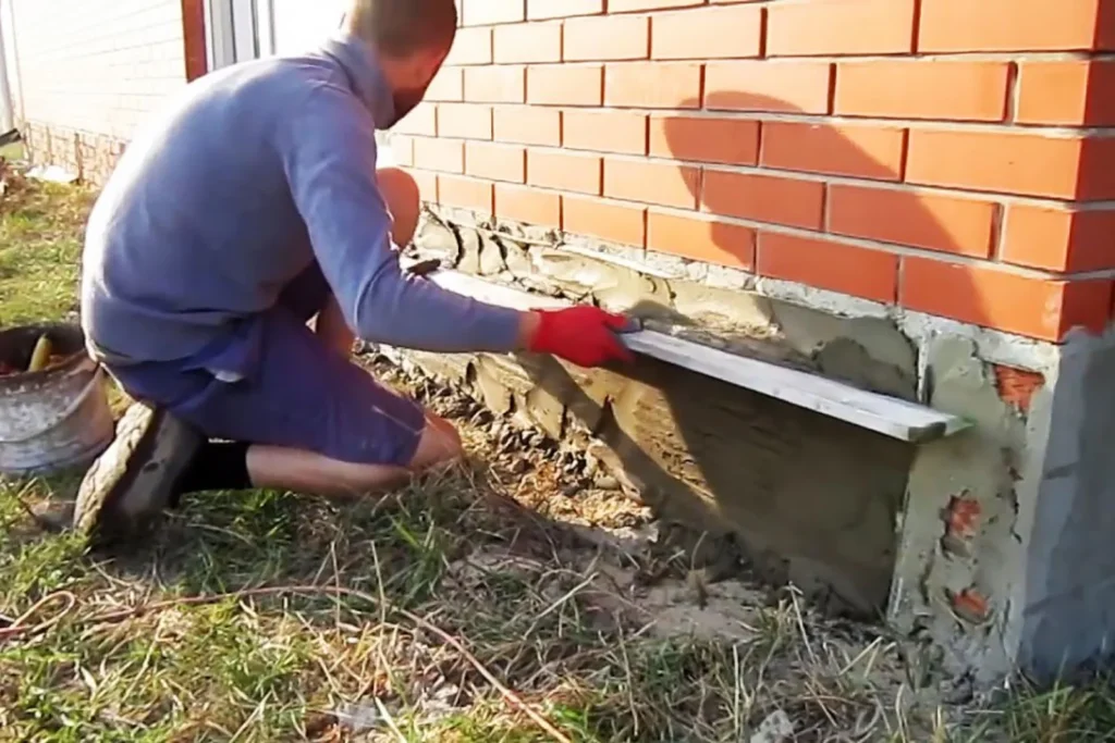 Worker applying parging to the base of a brick wall
