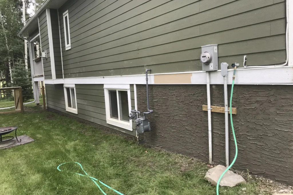 Dark textured parging on a raised foundation below siding
