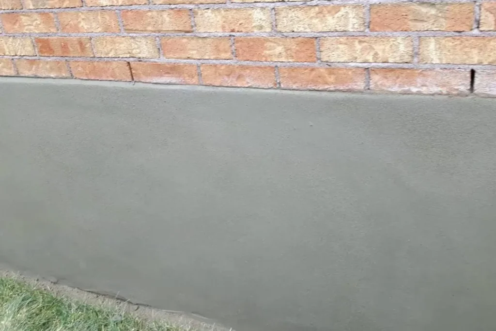 Smooth grey parging on a foundation below a red brick wall