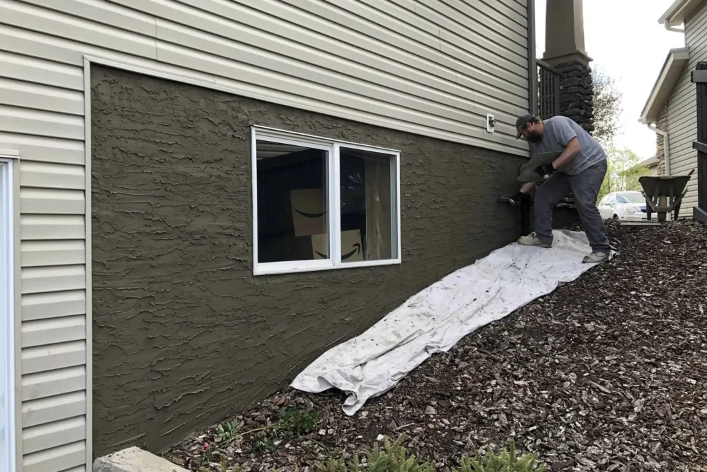 Worker applying textured parging around a basement window