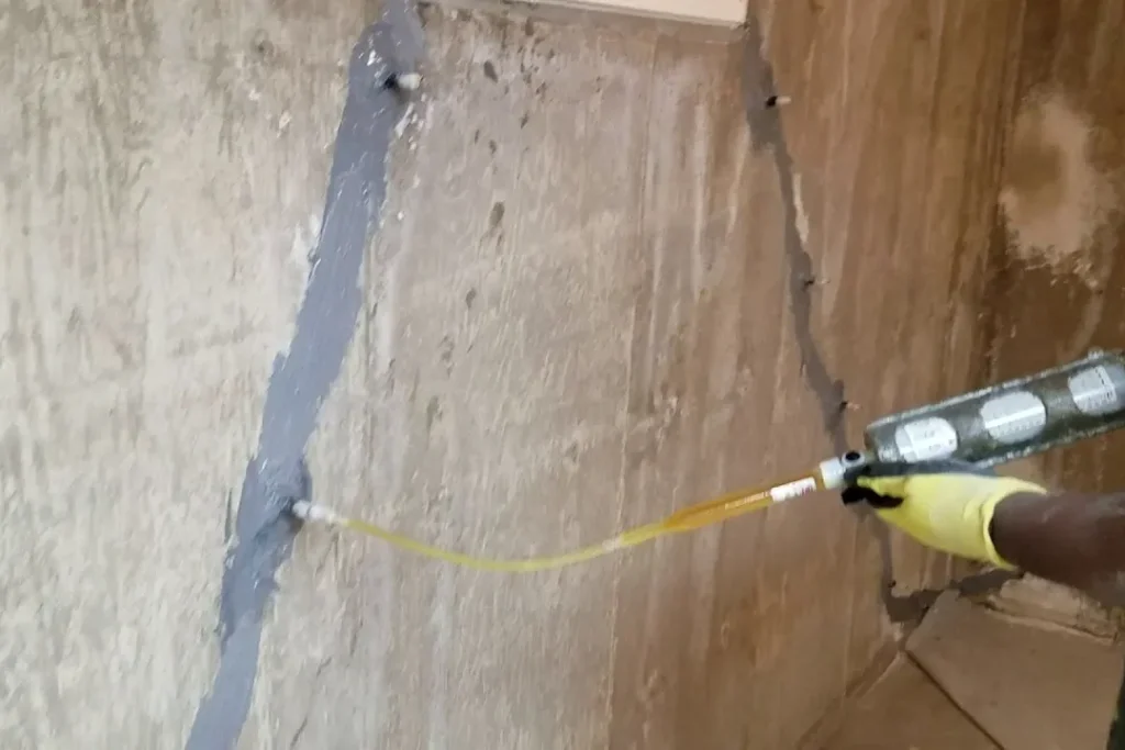 Gloved hand injecting filler into sealed cracks on a concrete foundation wall