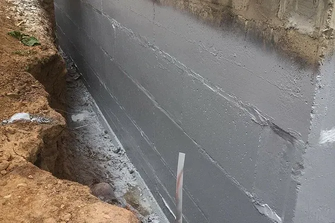 Grey parge coat on a block foundation beside an open trench