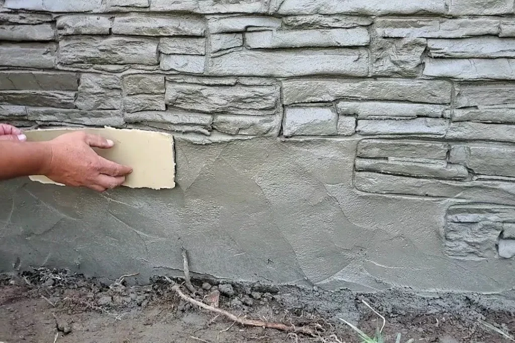 Hand pressing a stamp into fresh parging beside a stone-pattern finish