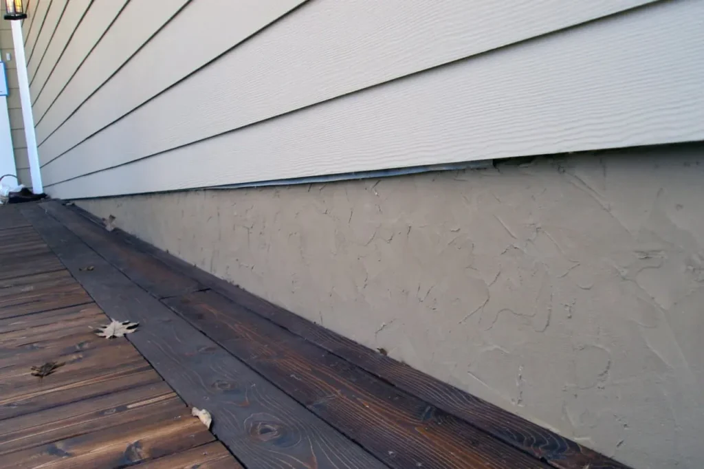 Light textured parging on a foundation beside a wooden deck
