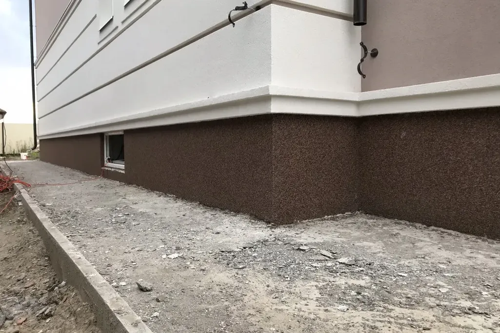 Brown speckled textured finish on a foundation below a white wall