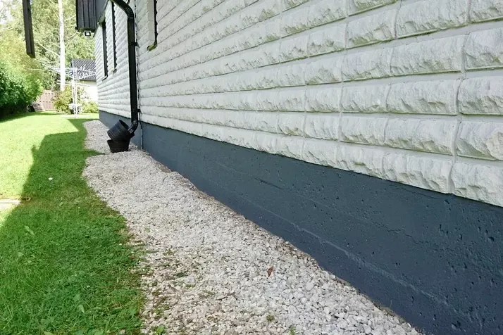 Smooth dark grey parging on a foundation beside a gravel strip and lawn
