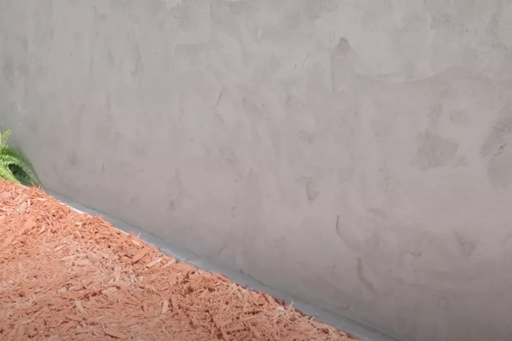Smooth finished parging on a foundation wall above red mulch