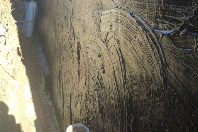 Black waterproof coat on a foundation in an open trench beside a brick house