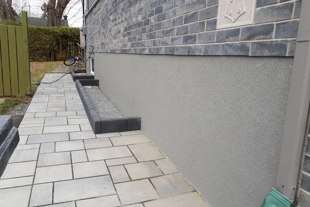 Smooth light grey parging on a tall foundation band below brick beside a stone walkway