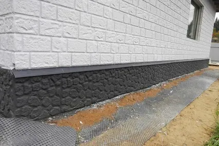 Dark stone-pattern parging on a foundation below light siding