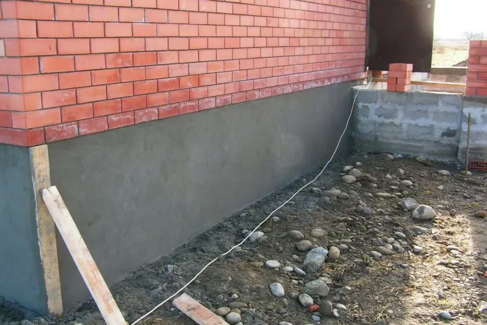 Fresh grey parging on a foundation below a red brick wall