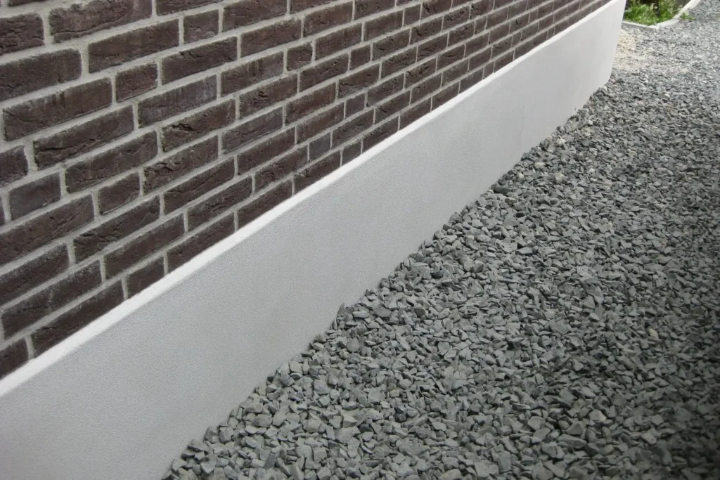 Light grey parging band below dark brick beside a slate gravel bed