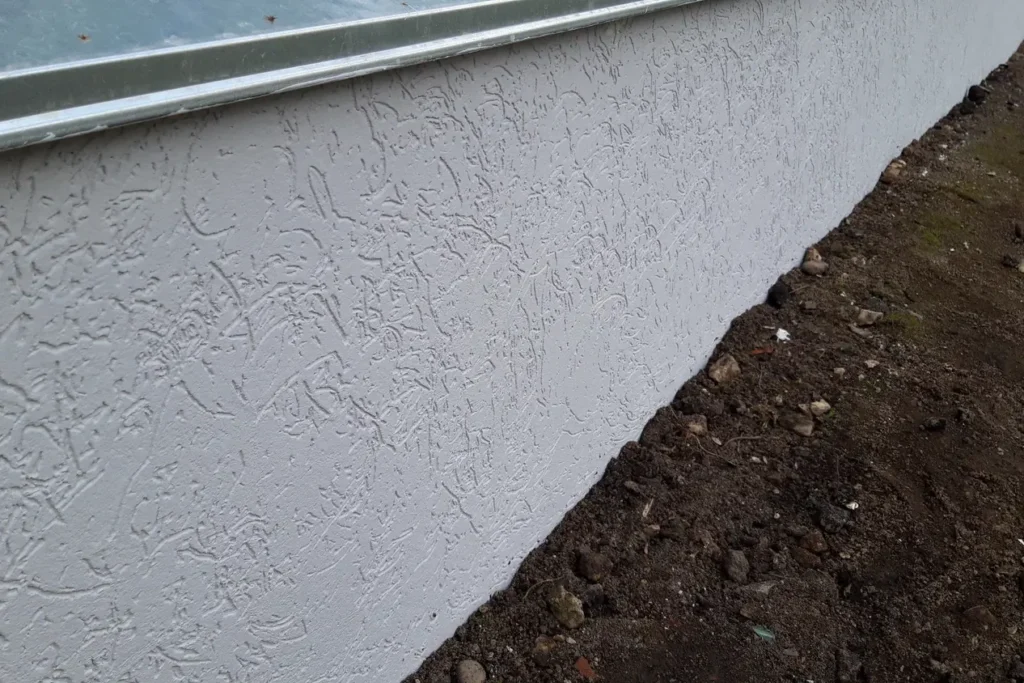 Light grey textured parging below metal flashing on a foundation