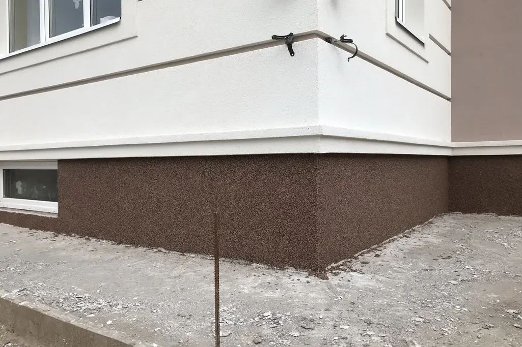 Brown speckled textured finish on a foundation corner below a white wall