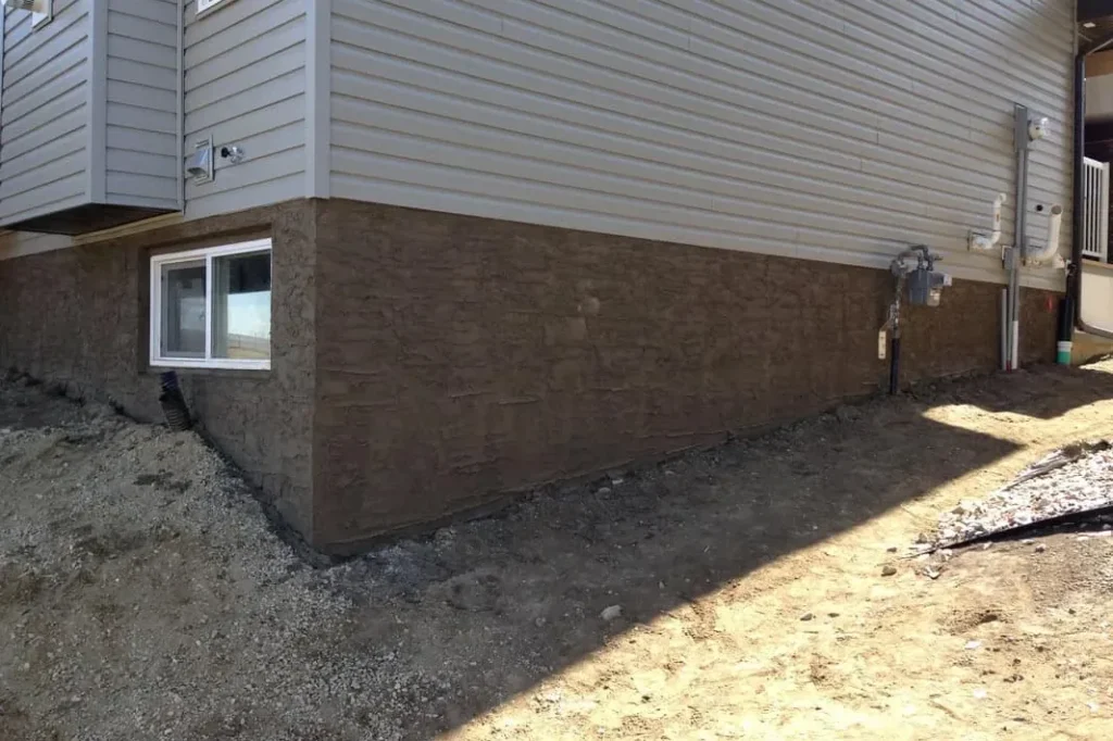 Stone-pattern parging on the foundation of a newer house with vinyl siding