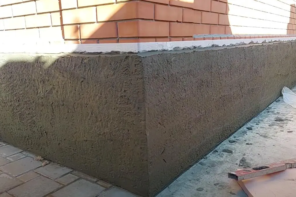Textured parging wrapped around a foundation corner below brick