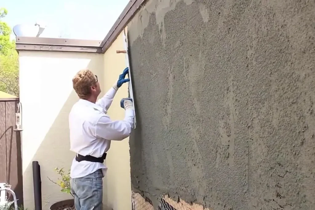 Worker troweling a cement coat onto a wall over wire mesh