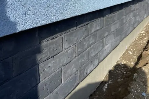 Dark stone-pattern parging along a foundation below a light blue stucco wall