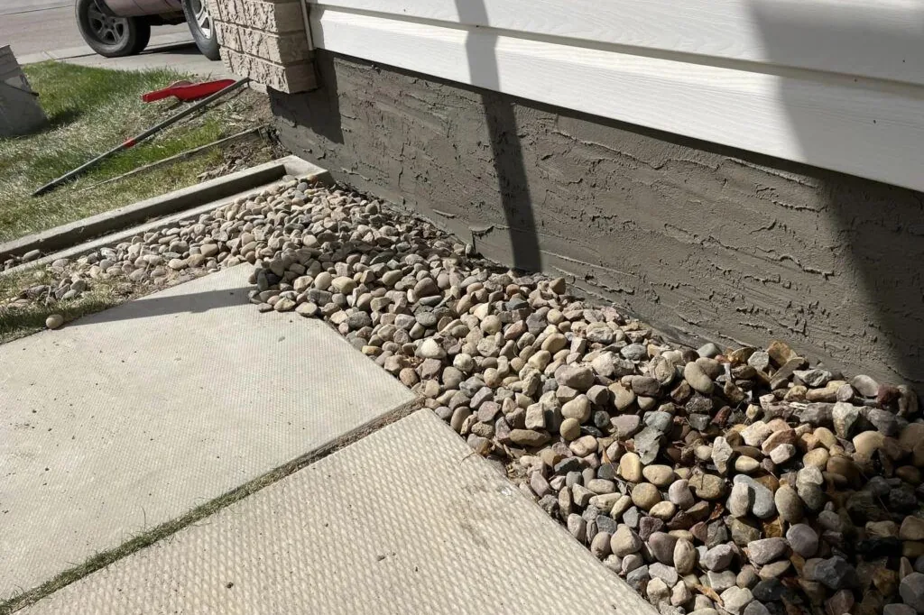 Textured grey parging on a foundation above a river-rock bed