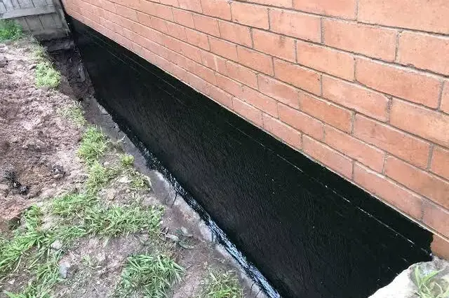Fresh black waterproof coating on a foundation below a red brick wall