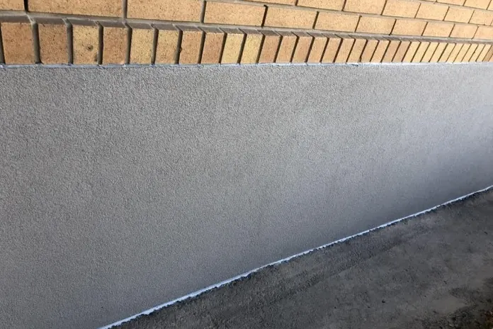 Fresh fine-textured grey parging on a foundation below a brick wall